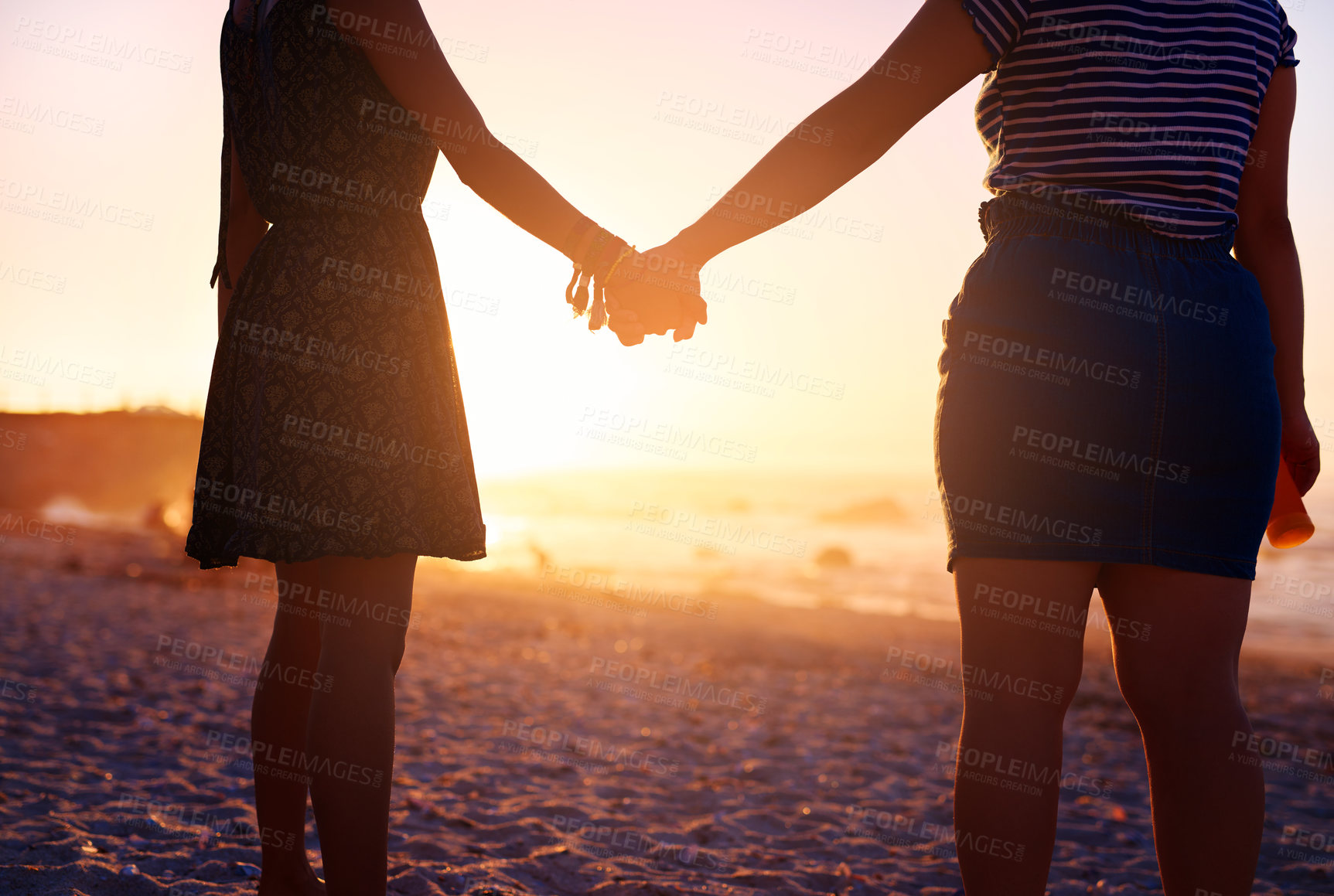 Buy stock photo Rearview shot of two unrecognizable young women holding hands on the beach at sunset