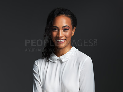 Buy stock photo Portrait of an attractive young woman wearing a white blouse and smiling against a dark background in the studio