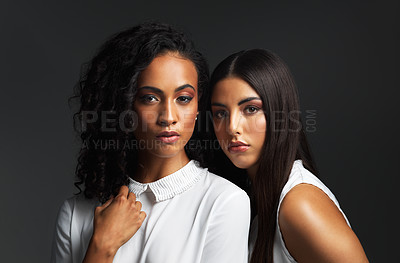 Buy stock photo Portrait of two attractive young women wearing white blouses posing closely together against a dark background in the studio