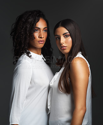 Buy stock photo Studio shot of two attractive young women wearing white blouses posing closely together against a dark background