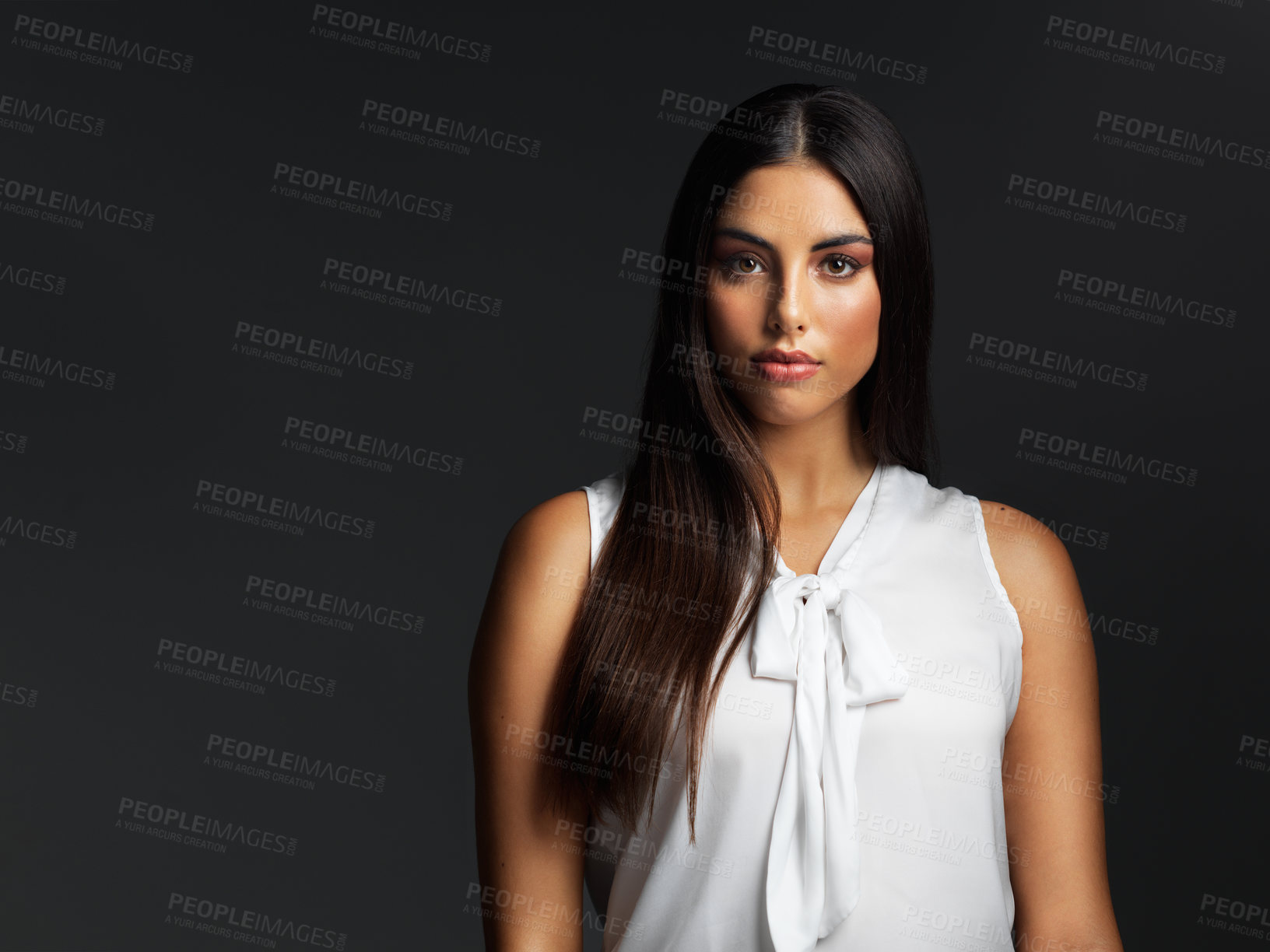 Buy stock photo Portrait of an attractive young woman wearing a white blouse and posing against a dark background in the studio