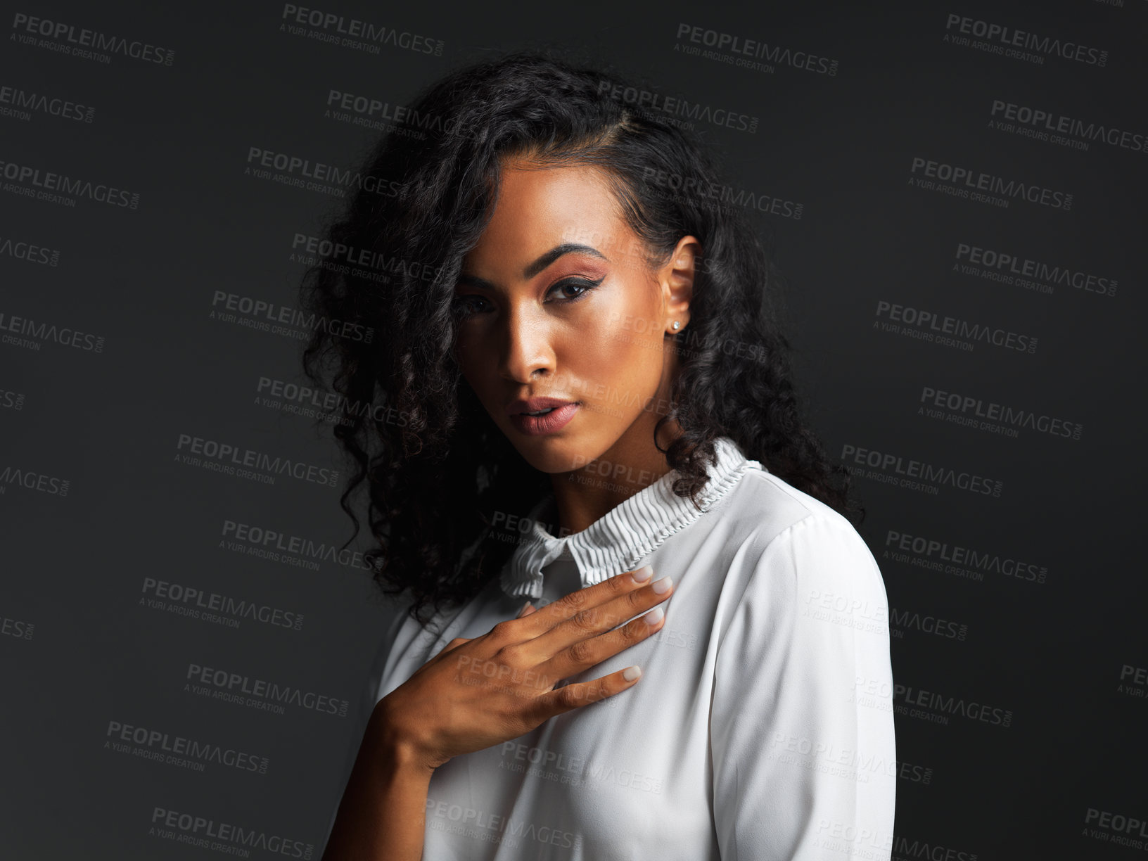 Buy stock photo Portrait of an attractive young woman wearing a white blouse and posing seductively against a dark background in the studio