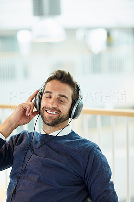Buy stock photo Shot of a young businessman listening to music in an office