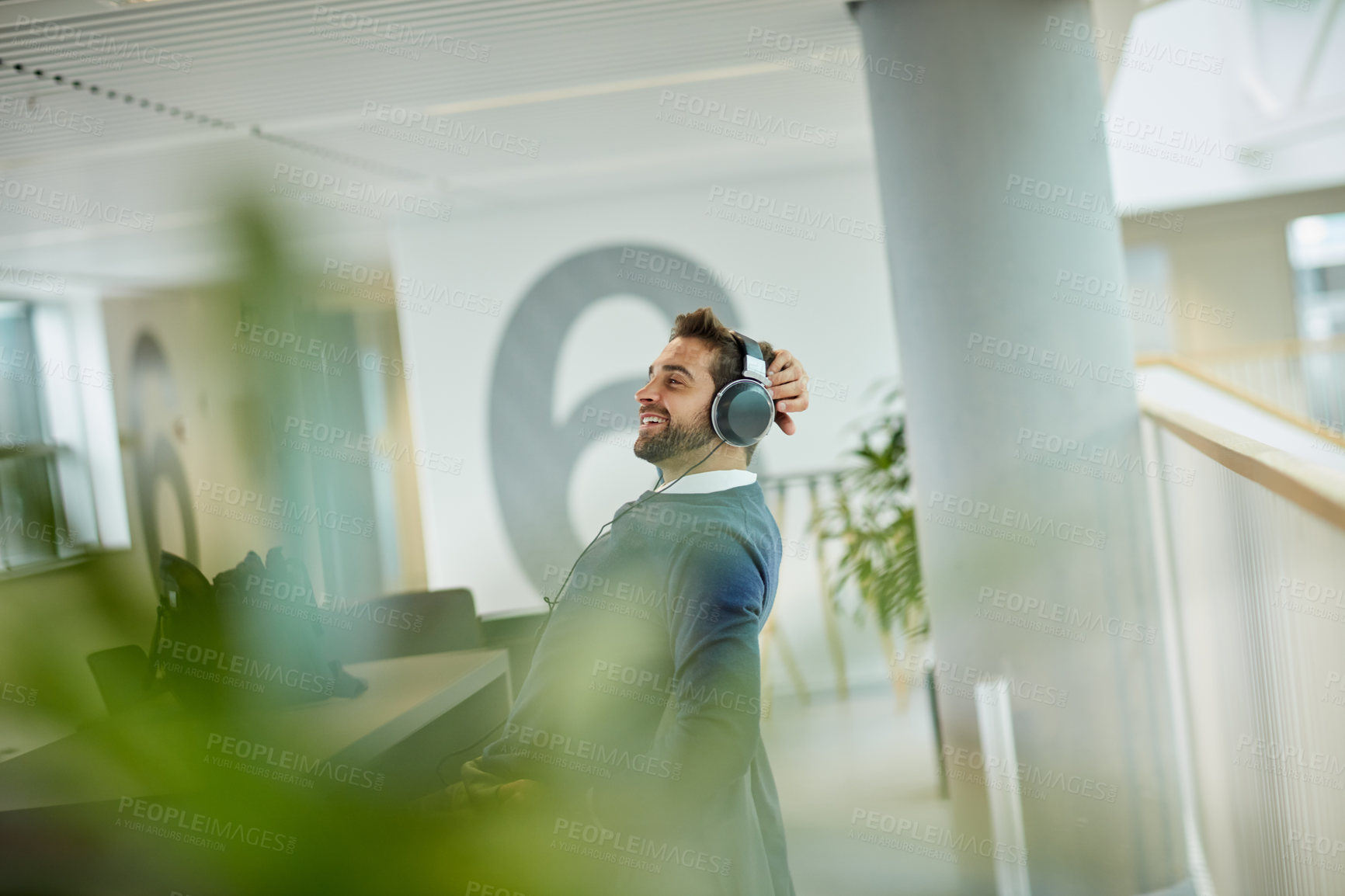 Buy stock photo Shot of a young businessman listening to music in an office