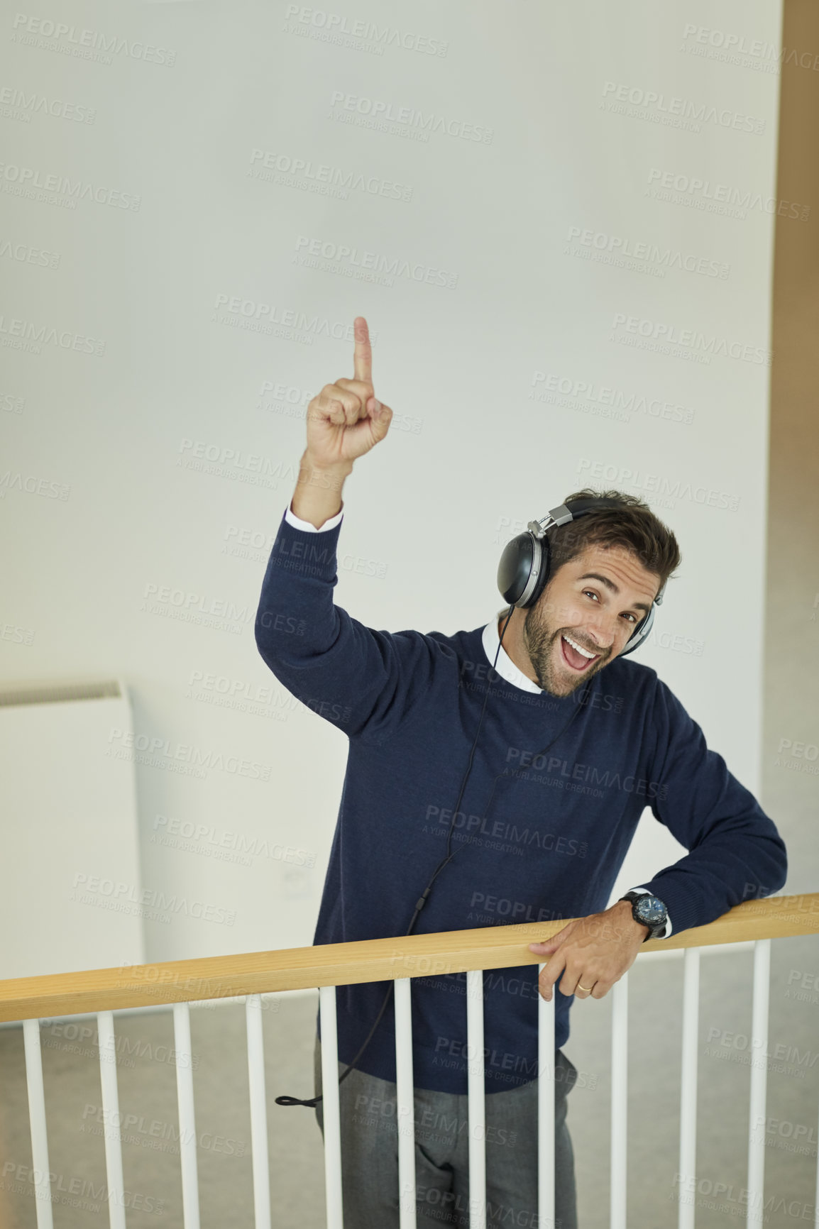 Buy stock photo Portrait of a young businessman wearing headphones and pointing up in an office