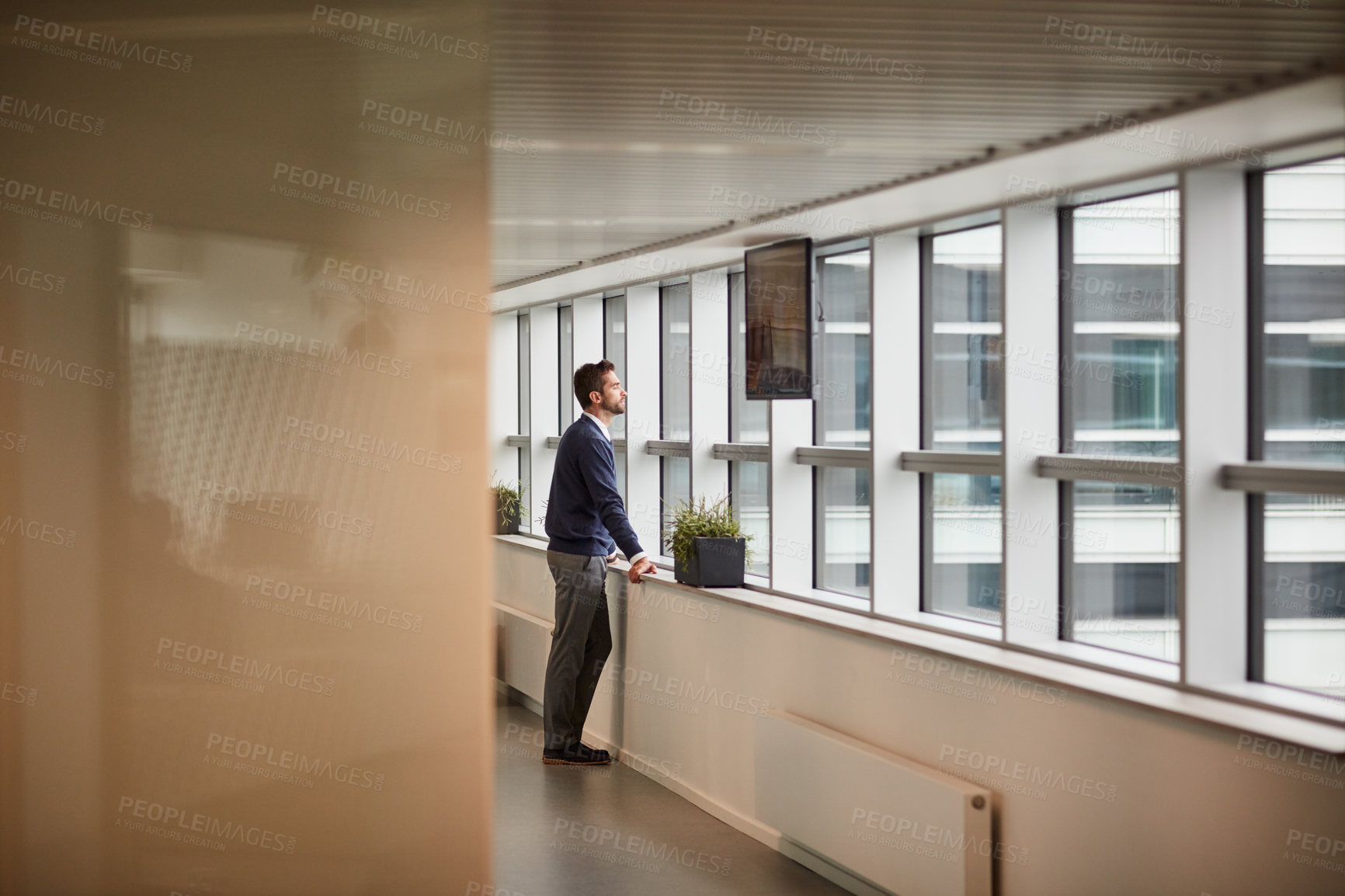 Buy stock photo Shot of a young businessman looking through a window in an office