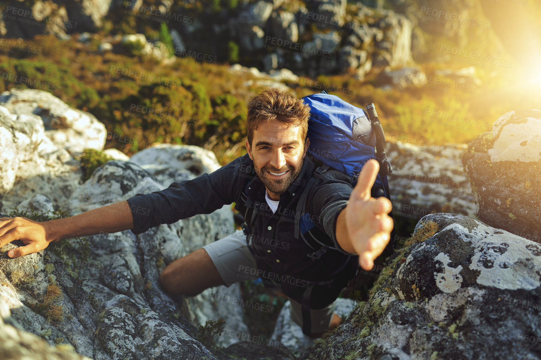 Buy stock photo Shot of a young man extending his hand to help while hiking up a mountain
