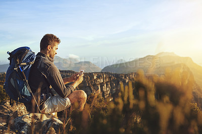 Buy stock photo Shot of a young man using a smartphone while hiking up a mountain