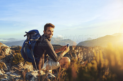 Buy stock photo Shot of a young man using a smartphone while hiking up a mountain