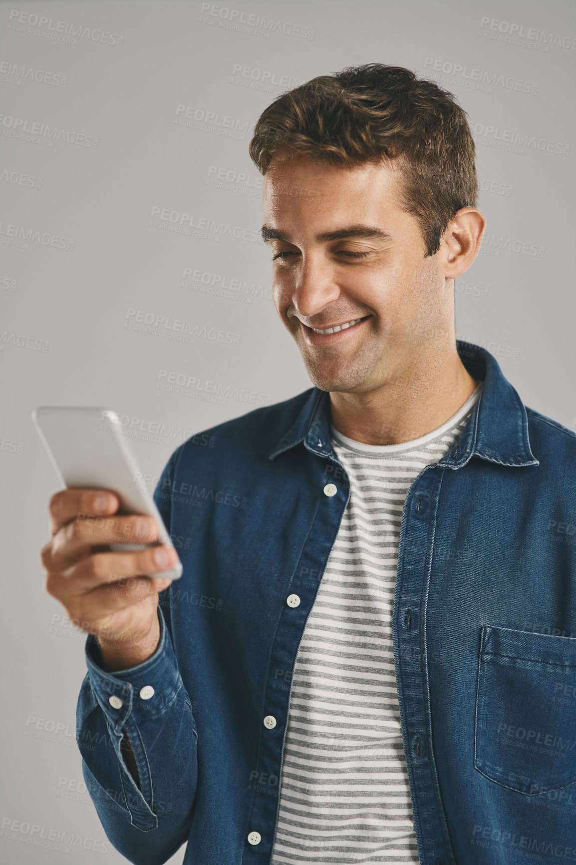 Buy stock photo Studio, man and cellphone for chatting, networking and funny news with contact on social media. Creative worker, scroll and browse on dating app with humor, text and connection by gray background