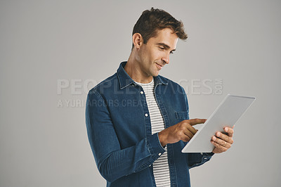 Buy stock photo Studio shot of a young man using a digital tablet against a grey background
