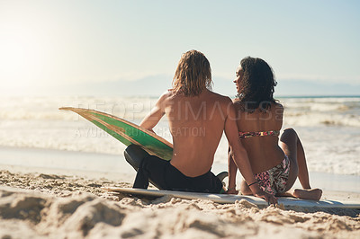 Buy stock photo Shot of a young couple sitting on the beach with their surfboards