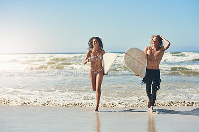 Buy stock photo Shot of a young couple spending the day at the beach with their surfboards