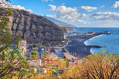 Buy stock photo Beautiful ocean coastline with black beach sand on Puerto de Tazacorte. Colorful town houses or tourism holiday resort accommodation near a mountain and seaside in La Palma, Spain