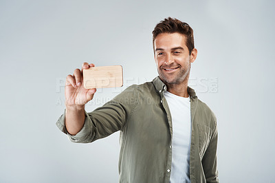 Buy stock photo Studio shot of a cheerful young man taking a self portrait with his cellphone while standing against a grey background