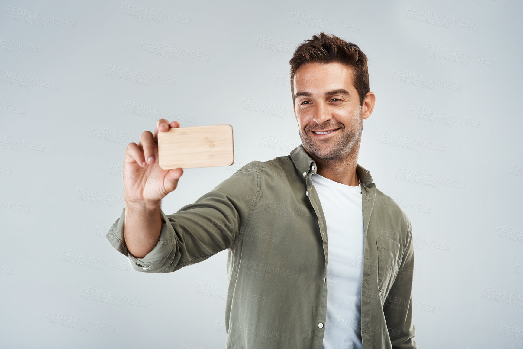 Buy stock photo Studio shot of a cheerful young man taking a self portrait with his cellphone while standing against a grey background