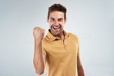 Buy stock photo Portrait of a cheerful young man punching the air in excitement while standing against a grey background