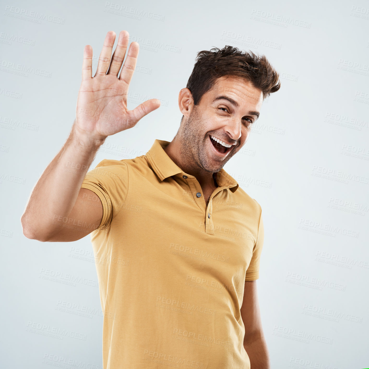 Buy stock photo Portrait of a cheerful young man smiling brightly with his one hand in the air while standing against a grey background