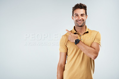 Buy stock photo Portrait of a cheerful young man pointing with his finger behind hime while standing against a grey background