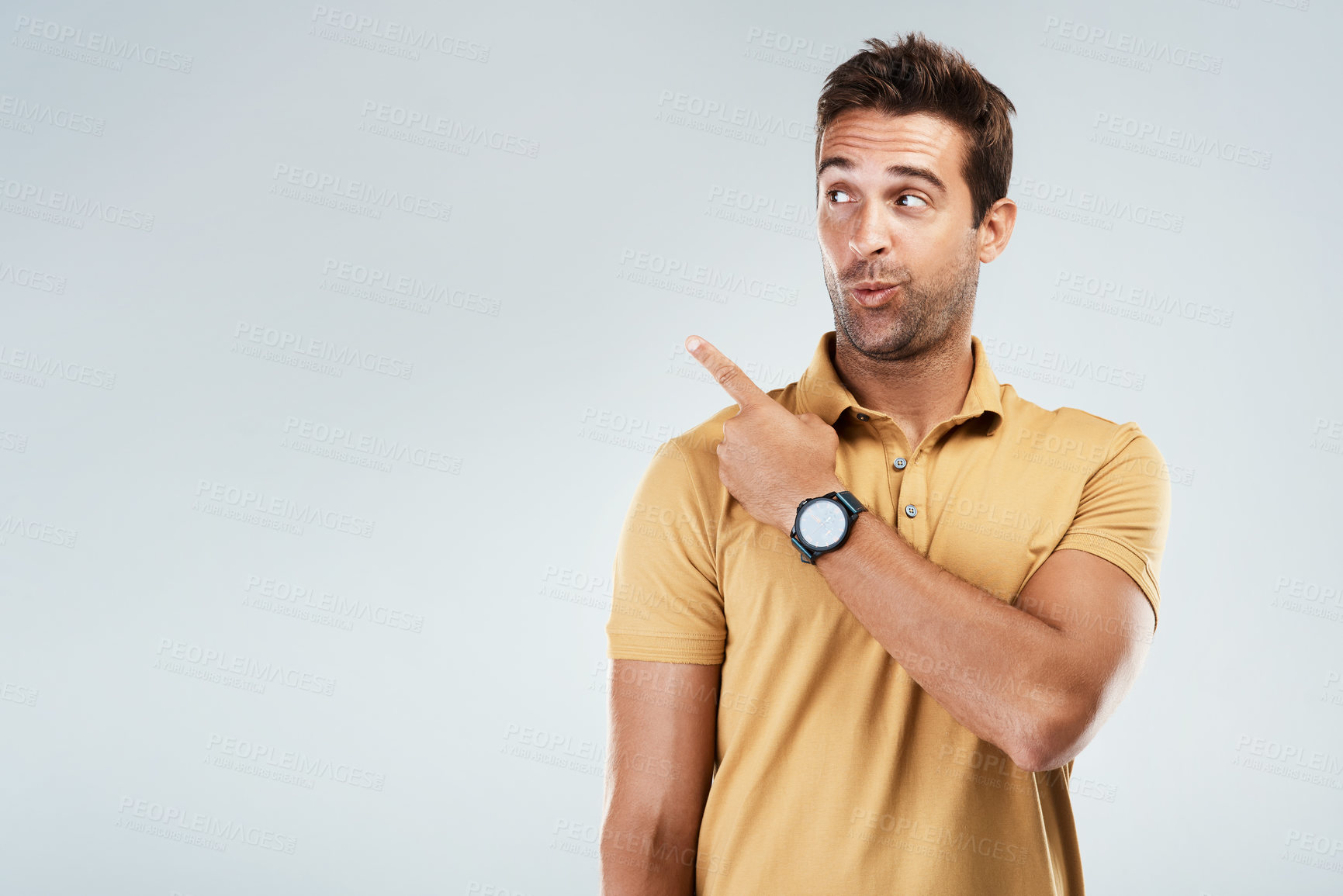 Buy stock photo Studio shot of a cheerful young man pointing with his finger behind hime while standing against a grey background