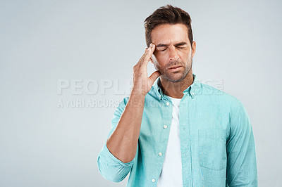 Buy stock photo Studio shot of a young man with an uncomfortable facial expression due to a headache while standing against a grey background
