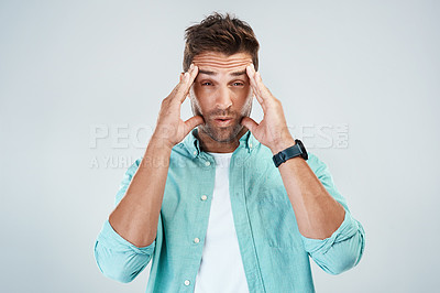 Buy stock photo Studio shot of a young man with an uncomfortable facial expression due to a headache while standing against a grey background