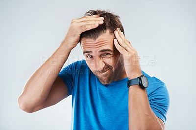 Buy stock photo Portrait of a young man with a confused facial expression taking a closer look at his hair while standing against a grey background