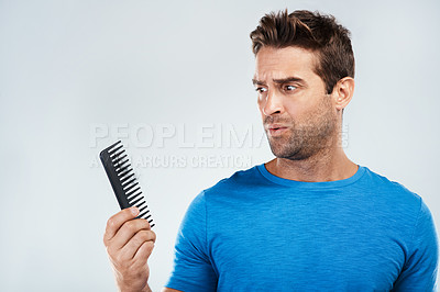 Buy stock photo Studio shot of a young man with a confused facial expression holding and looking at a hair comb while standing against a grey background