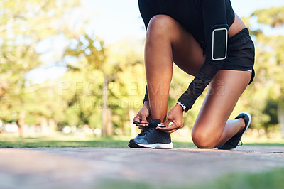 Buy stock photo Cropped shot of an unrecognizable young woman tying her shoe laces before her run in the park during the day