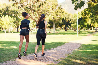 Buy stock photo Rearview shot of two attractive young women running next to each other in the park during the day