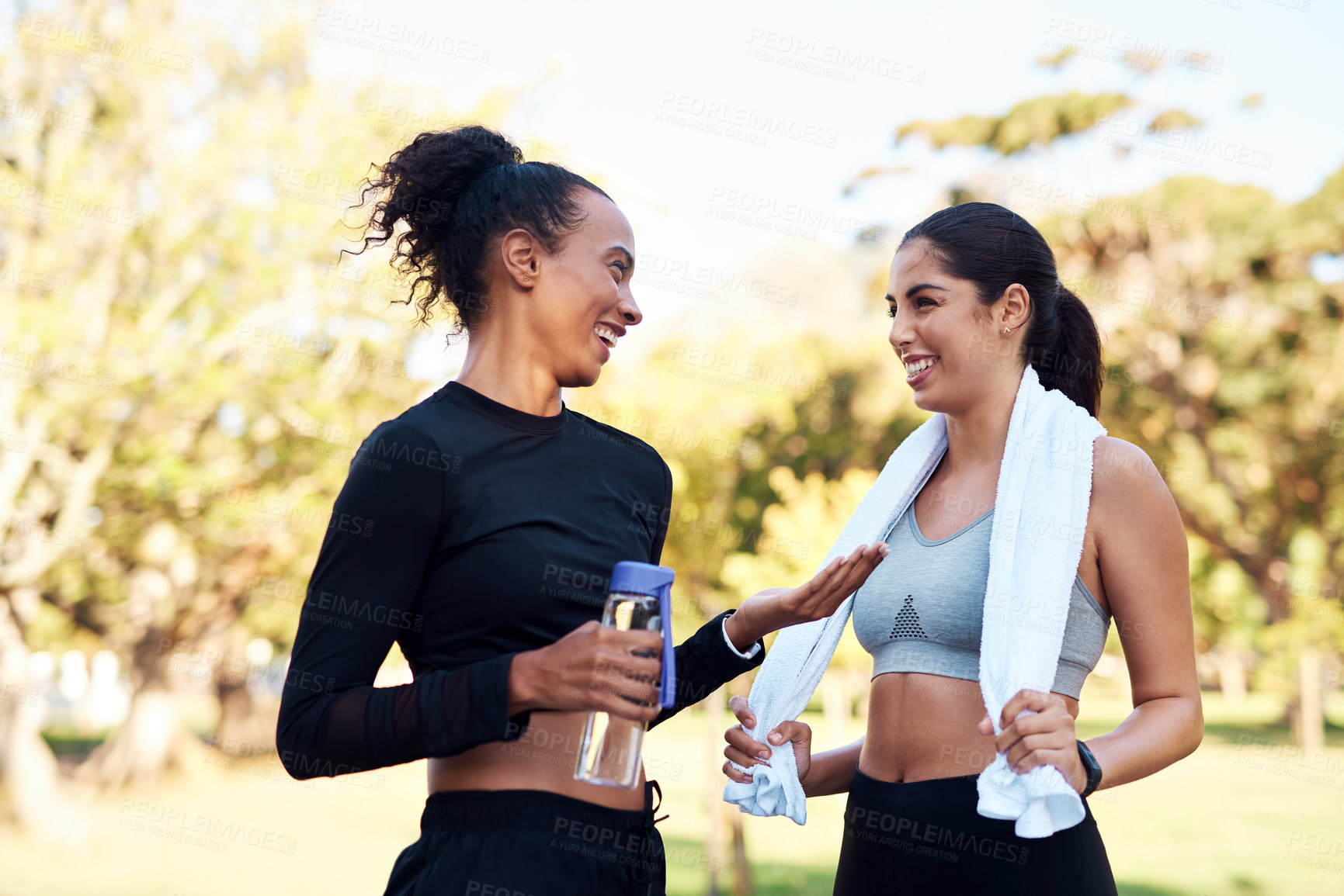 Buy stock photo Cropped shot of two attractive young women smiling at each other after their run in the park during the day