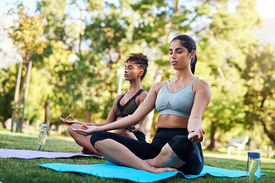 Buy stock photo Full length shot of two attractive young women sitting next to each other and meditating in the park