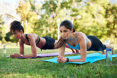 Buy stock photo Full length shot of two attractive young women holding a plank position in the park during the day