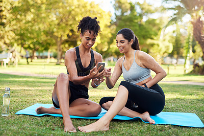 Buy stock photo Full length shot of two attractive young women sitting next to each other while using a cellphone in the park