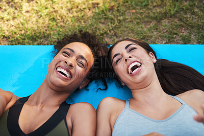 Buy stock photo Cropped shot of two attractive young women lying down on a yoga mat and laughing while outdoors