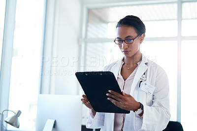 Buy stock photo Shot of a young doctor going over paperwork in her consulting room
