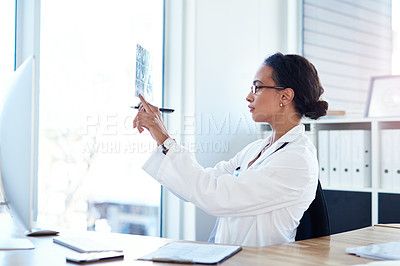 Buy stock photo Shot of a young doctor reading the results of an x ray in her consulting room
