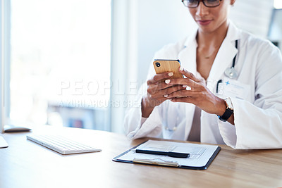 Buy stock photo Shot of a young doctor using a smartphone in her consulting room