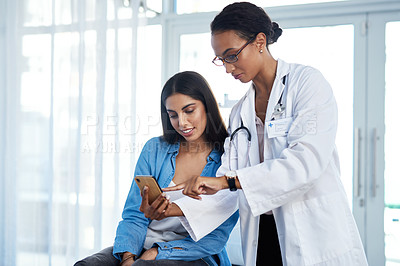 Buy stock photo Shot of a young doctor using a smartphone during a consultation with her patient