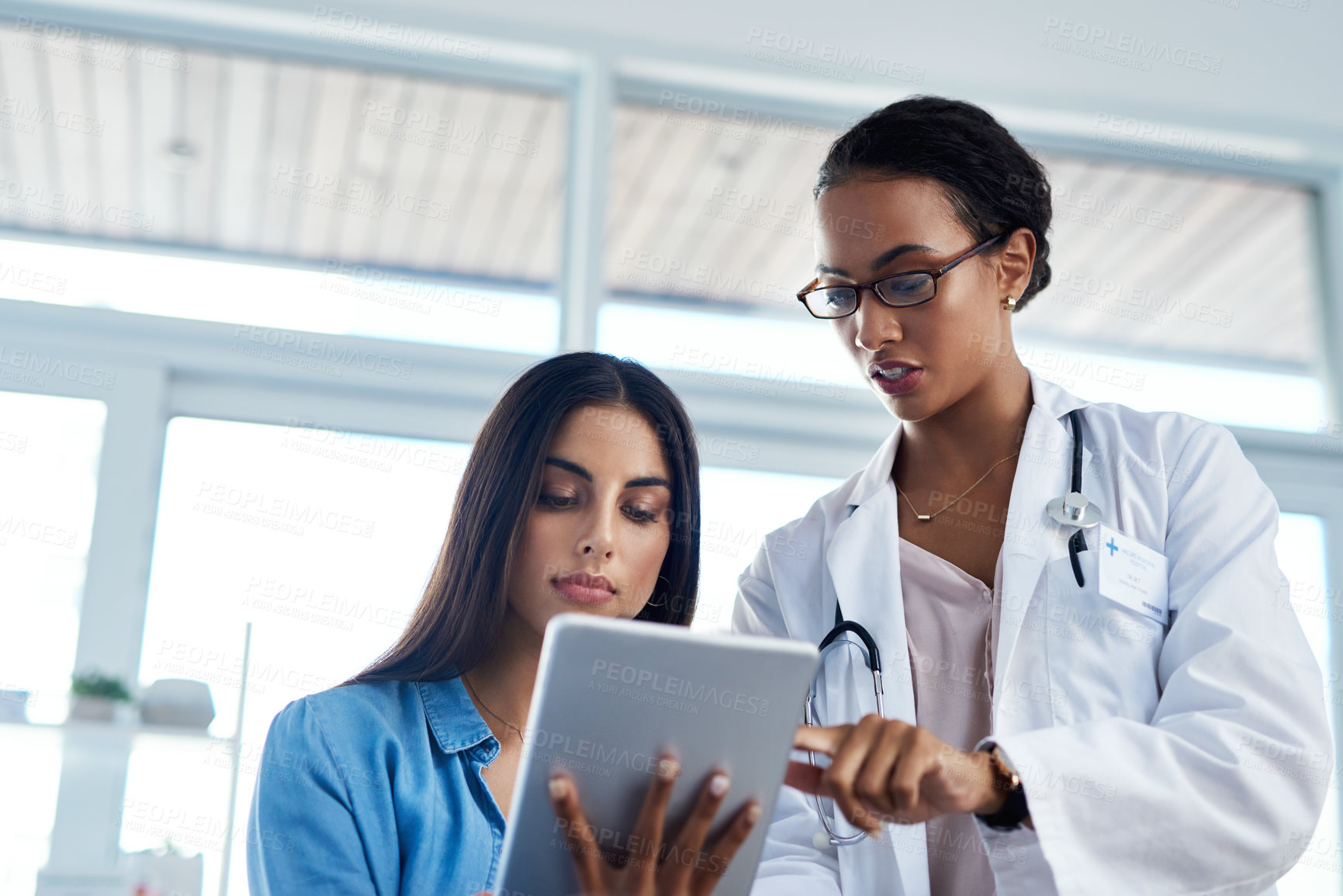 Buy stock photo Shot of a young doctor using a digital tablet during a consultation with her patient