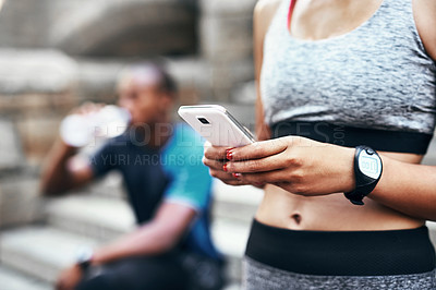 Buy stock photo Shot of an unrecognizable woman using her cellphone while exercising outdoors with her boyfriend resting in the background