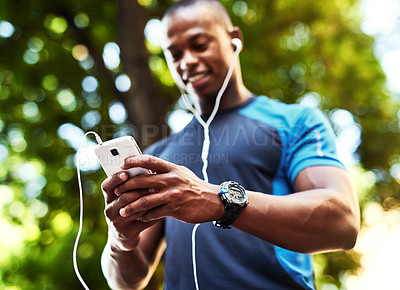 Buy stock photo Shot of a handsome young man listening to music and using his cellphone while exercising outdoors in the city