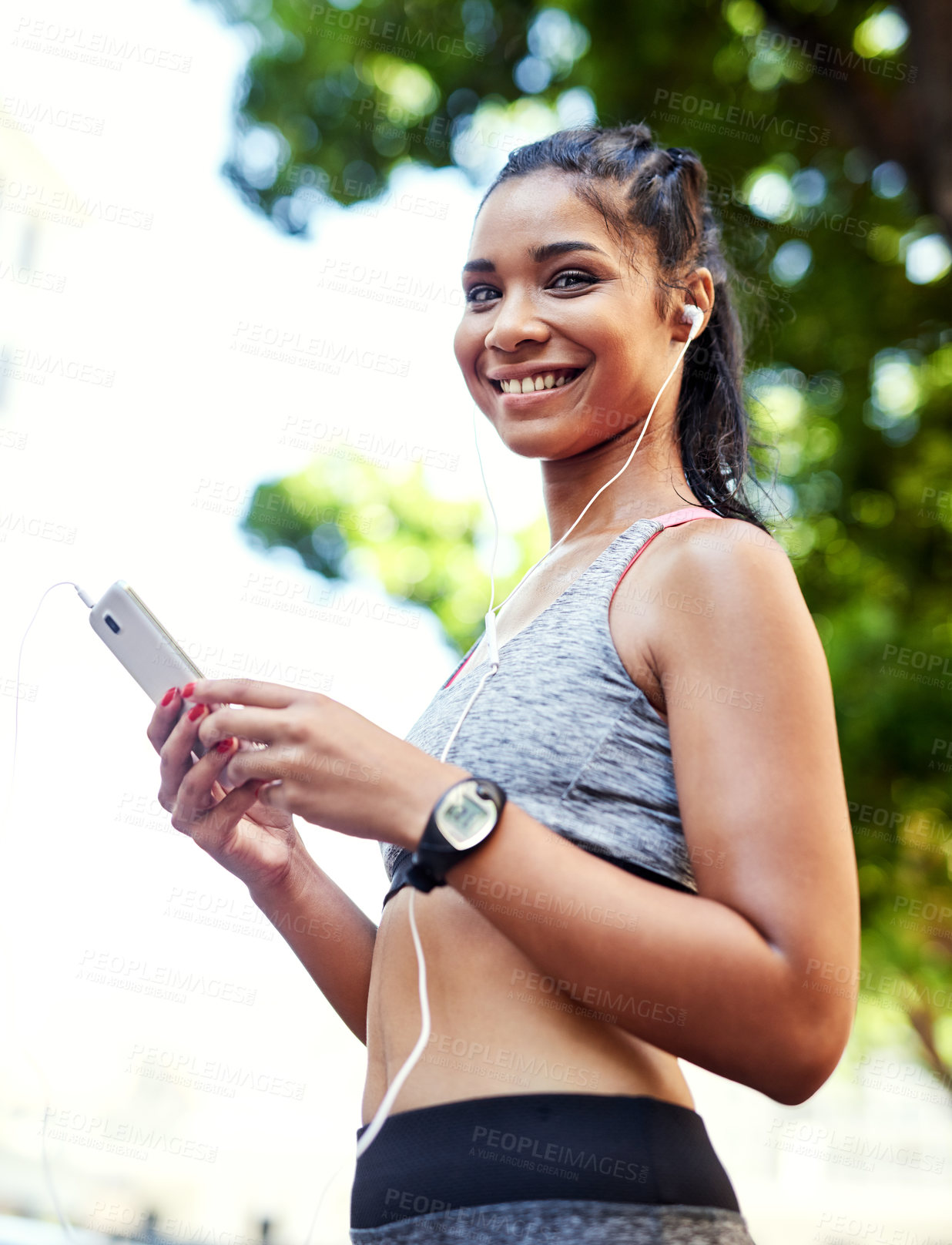 Buy stock photo Portrait of an attractive young woman listening to music and using her cellphone while exercising outdoors in the city