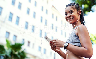 Buy stock photo Portrait of an attractive young woman listening to music and using her cellphone while exercising outdoors in the city