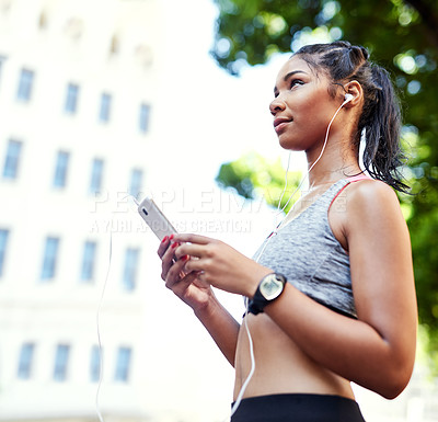 Buy stock photo Shot of an attractive young woman listening to music and using her cellphone while exercising outdoors in the city
