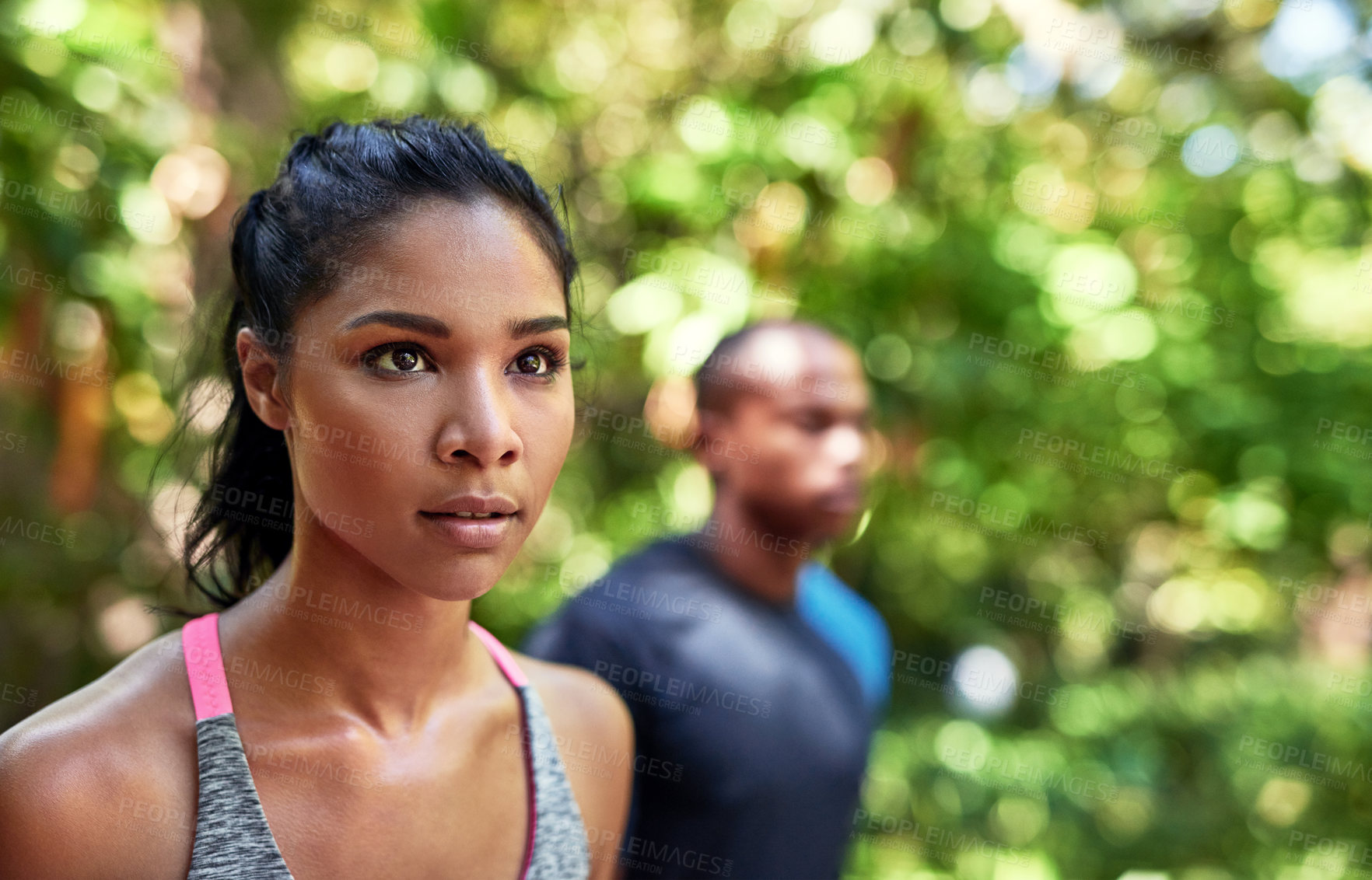 Buy stock photo Shot of an attractive young woman exercising outdoors with her boyfriend in the background