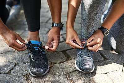 Buy stock photo Shot of an unrecognizable sporty couple tying their shoelaces while exercising outdoors