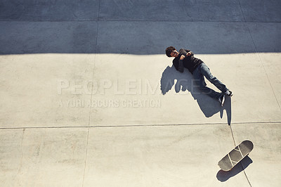 Buy stock photo High angle shot of a young man lying down on the floor next to his skateboard at a skatepark
