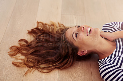 Buy stock photo Cropped shot of an attractive young woman lying down on the wooden floor in her living room during the day