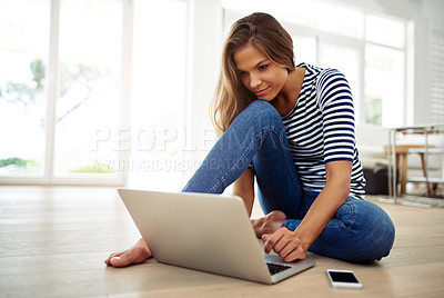 Buy stock photo Full body shot of an attractive young woman sitting and using a laptop in the living room during the day